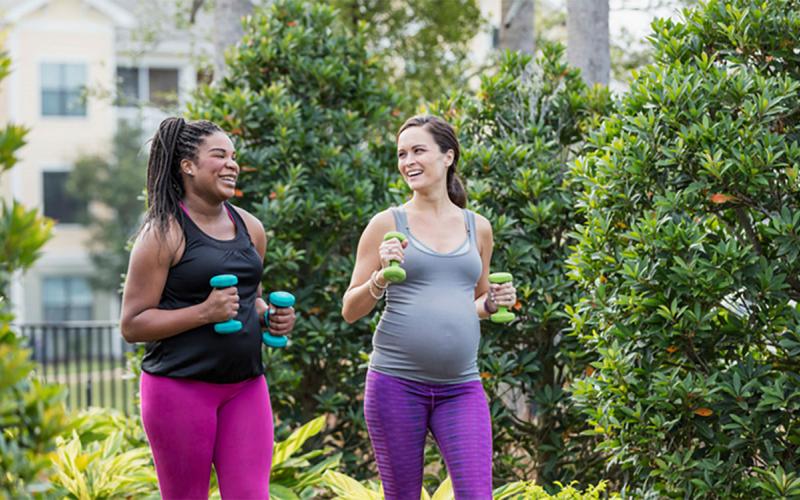 Two pregnant women exercising together, power walking.