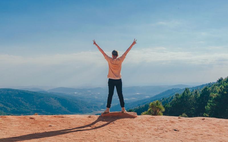 Young woman holding her arms in the air while overlooking a mountain range.