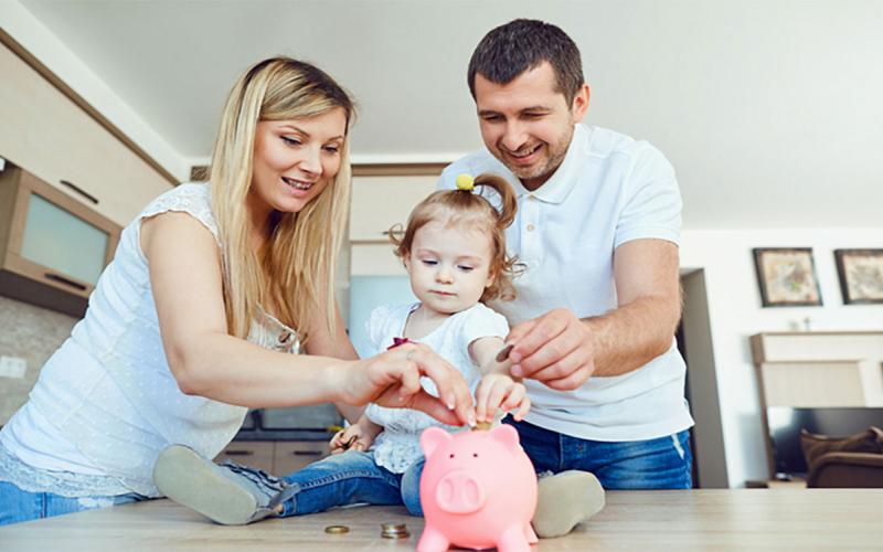 Mother, father, and daughter putting coins in a piggy bank.