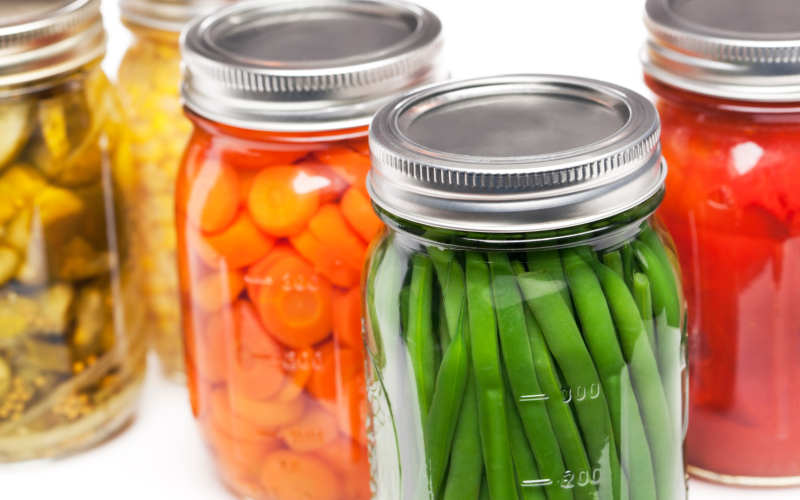 Jars of canned green beans, carrots, tomatoes, cucumbers and corn