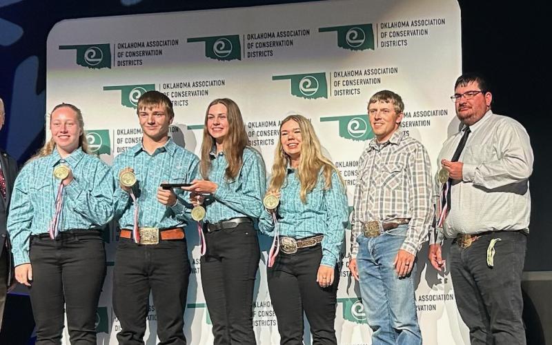 A team of four people in matching blue button-down shirts stands on stage with their awards, with two people off to the right side