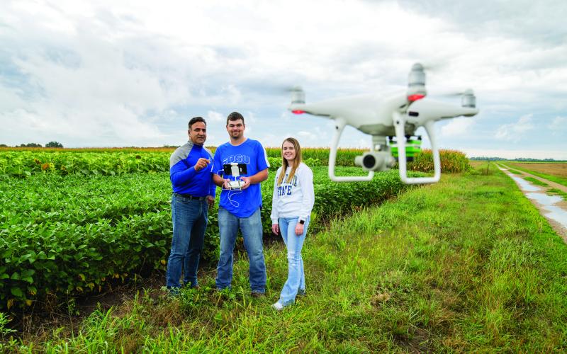 professor and two students use a drone to analyze a field