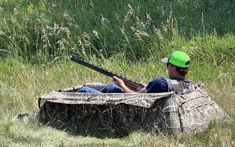 A youth sits in a hunting blind holding a shotgun