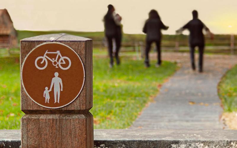 Sign posted alongside a rural walking and biking path with a family walking in the distance.