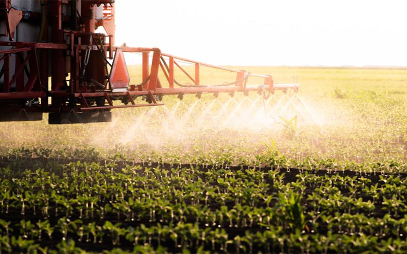Tractor applying postemergence herbicide to a soybean field early in the growing season.