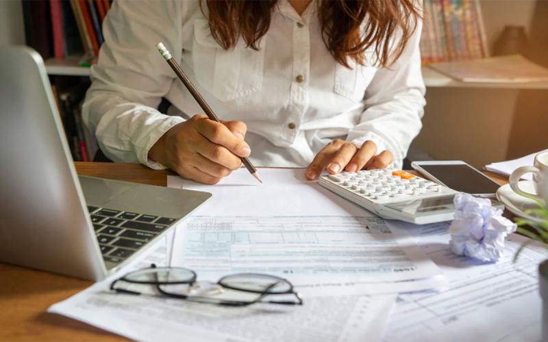 Young woman sitting at a laptop computer. She is reviewing a collection of bills.
