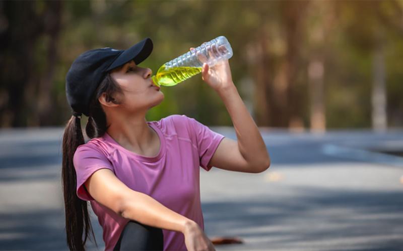 Woman taking a break to drink a sports drink while exercising outdoors.