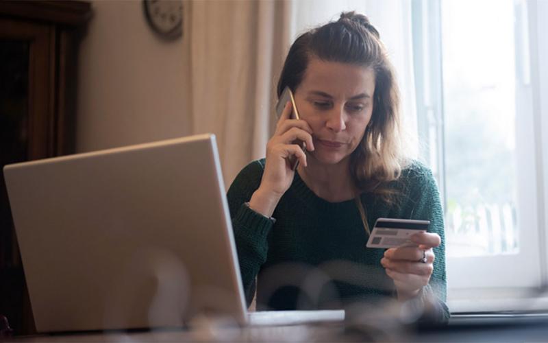 Woman at a laptop holding a credit card while talking to a customer service agent.
