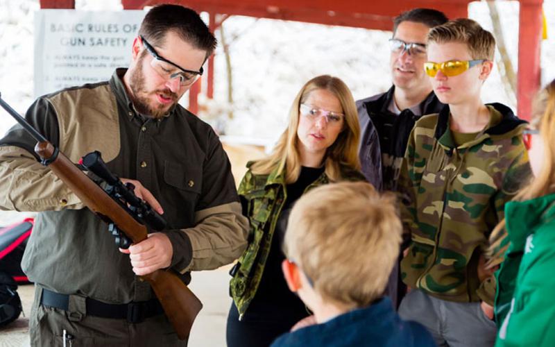 Shooting instructor demonstrating a rifle scope to a group of trainees.