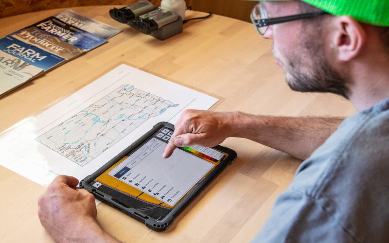 Young farmer at a table using smart device to review data and plan a customized seed application.