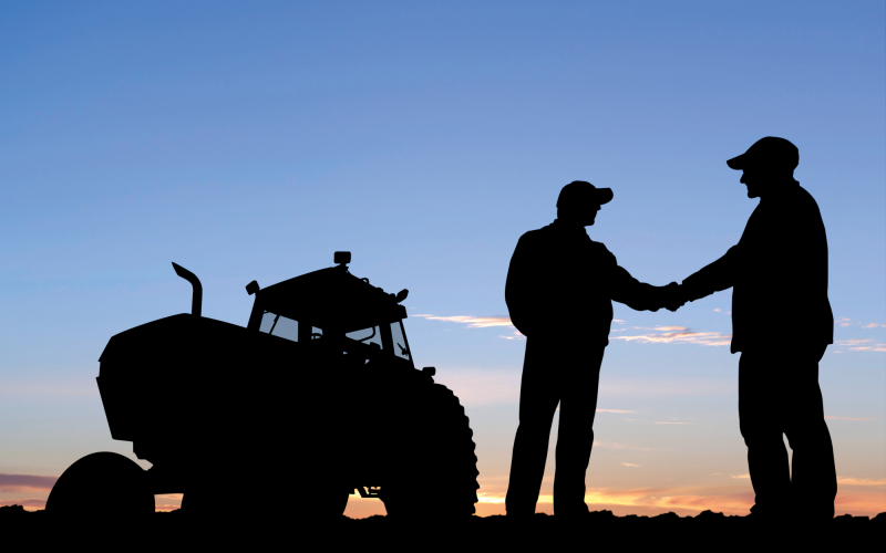 Sihlouette of farmers shaking hands with a tractor in the background