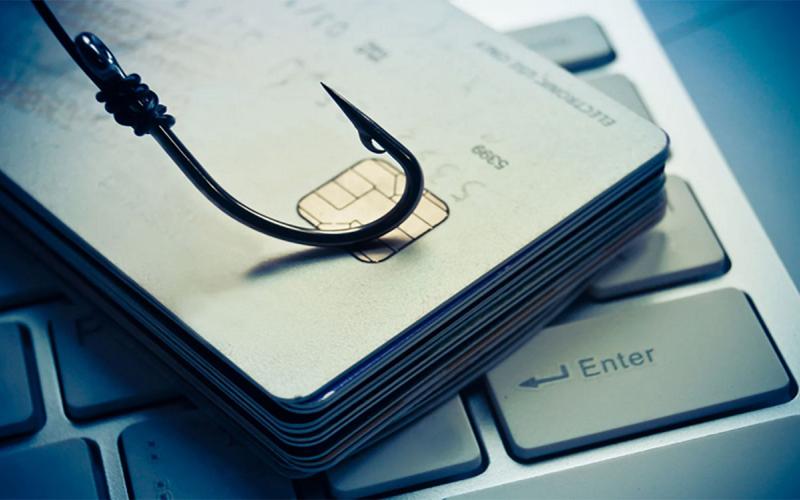 A fishing hook resting on a stack of credit cards on a laptop computer keyboard.