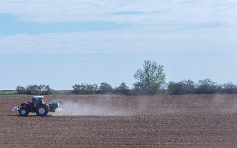 Tractor applying residual herbicide to a bare field.