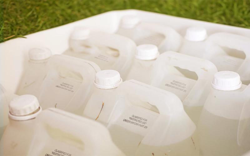 Several plastic bottles of pesticides gathered together in a white tub.
