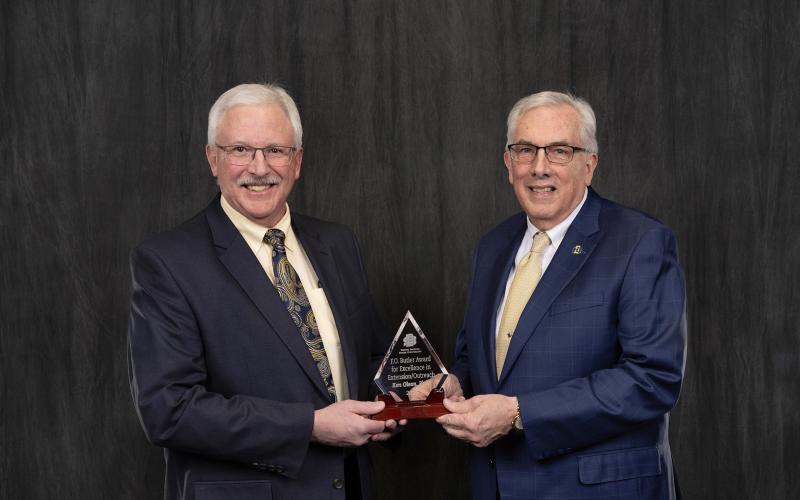 Two men smile for the camera holding a glass award