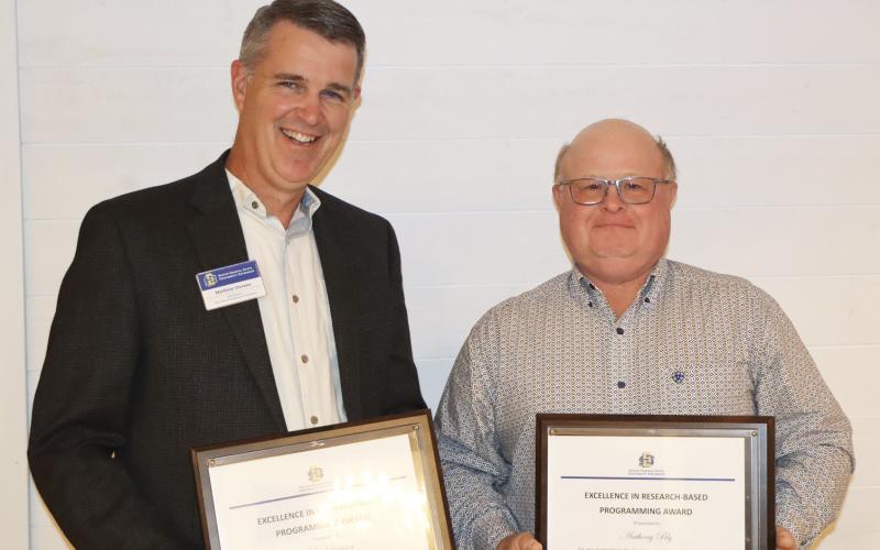 Two men smile for the camera while holding their plaques