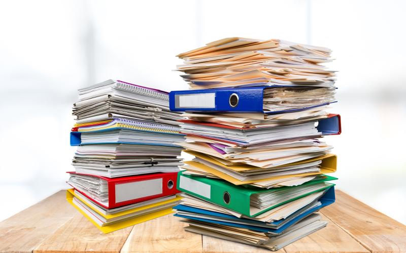 A stack of binders and file folders on a wood table.