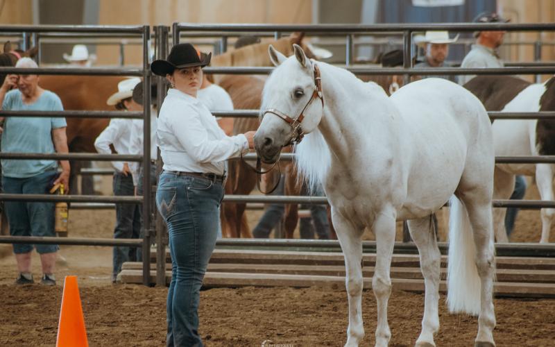 A girl in a black cowboy hat holds a white horse in a show ring