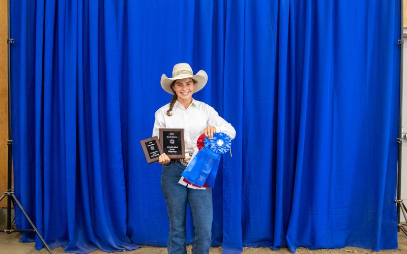 A girl in a cowboy hat holds two plaques and several large rosette awards
