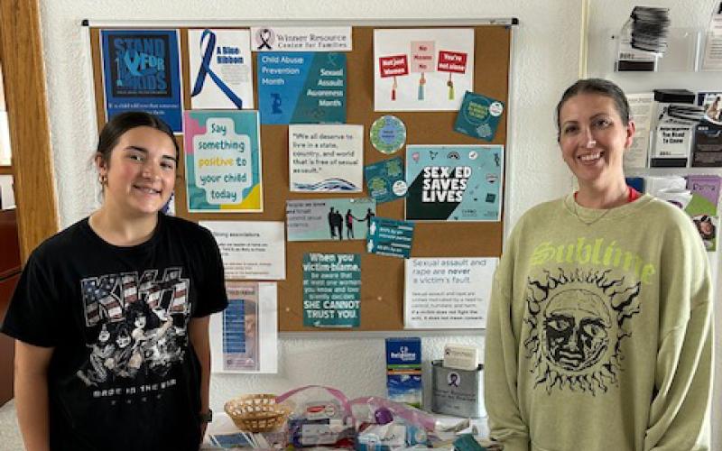 A girl and a woman stand on either side of a table stacked with donated hygiene items