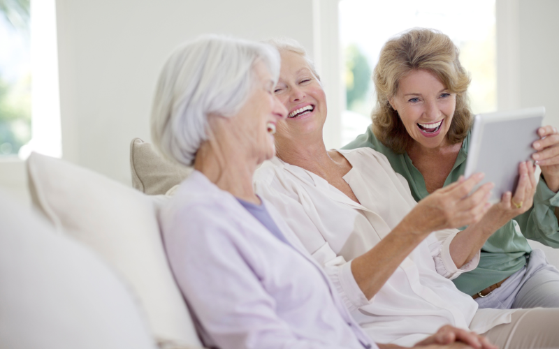 three older ladies laughing while looking at an iPad