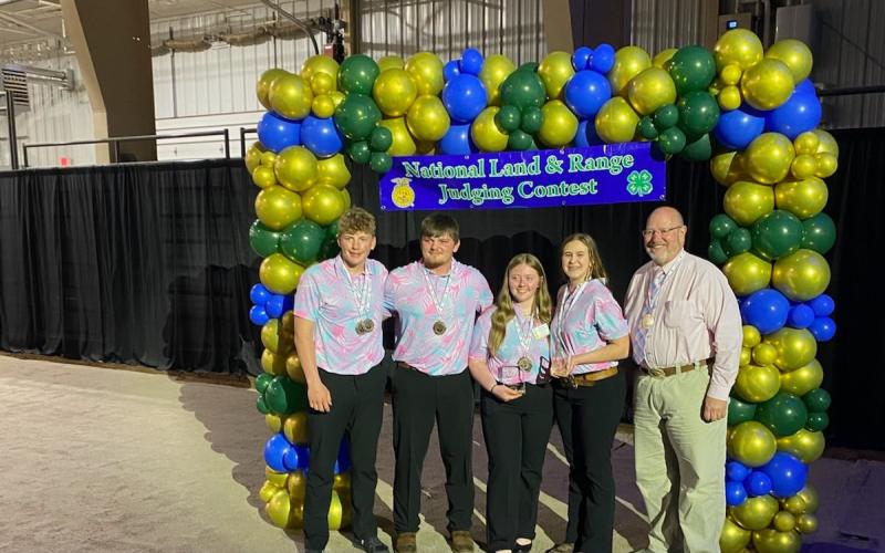 Four youth and an adult coach stand under a blue and green balloon arch