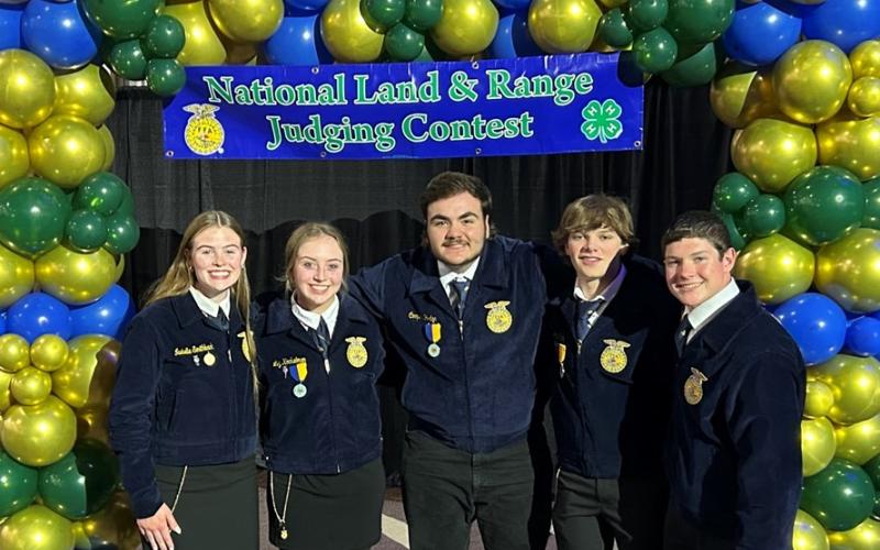 Five youth in FFA jackets stand under a blue and green balloon arch