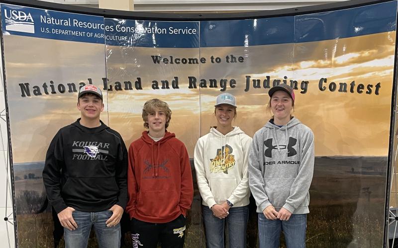 Four youth stand in front of a display that says "Welcome to the National Land and Range Judging Contest"