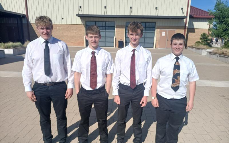 Four men in white button-down shirts, ties and black slacks stand outside for a team photo