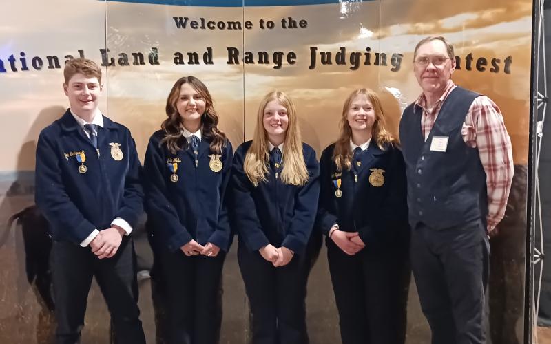 Four youth in blue FFA jackets and their coach pose for a team photo in front of a display that says "Welcome to the National Land and Range Judging Contest"