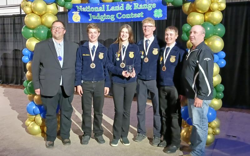 Four youth in blue FFA jackets wear medals around their neck and smile for a team photo with their coaches on either side