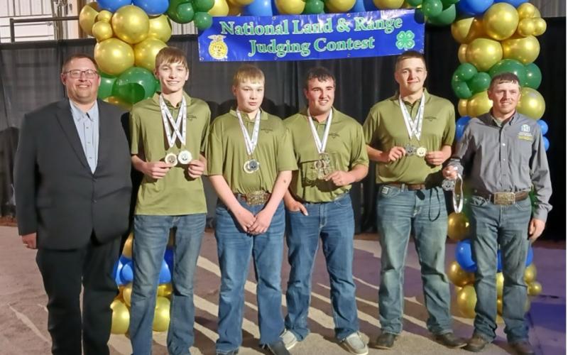 Four teenage boys in matching olive green shirts stand between their coaches wearing medals around their necks