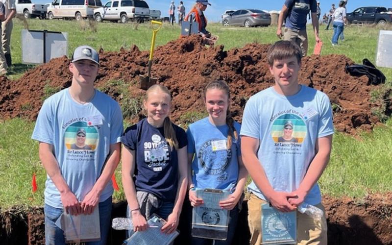 Four youth stand inside a shallow hole with clipboards used to evaluate a homesite