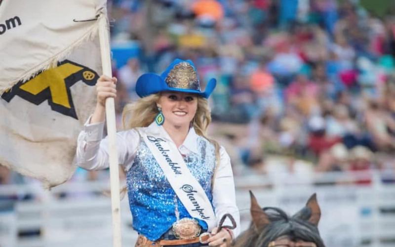 A woman wearing a cowboy hat with a crown rides a horse and carries a flag