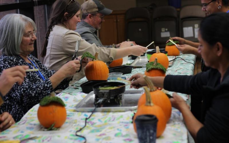 People sit at a long white table painting pumpkins