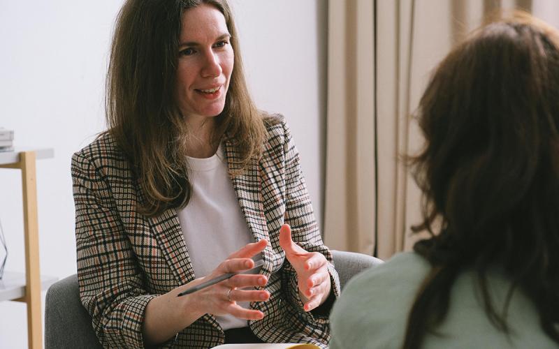 A therapist sitting with notebook and talking with a client.