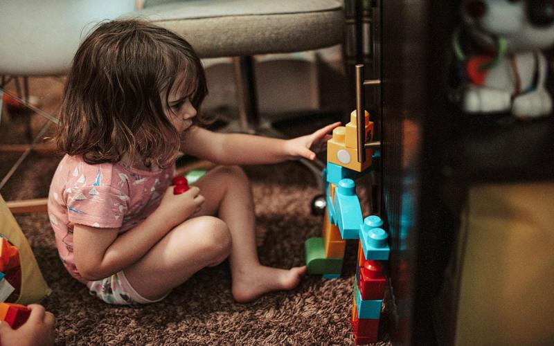 Child stacking blocks against an entertainment center in al living room.