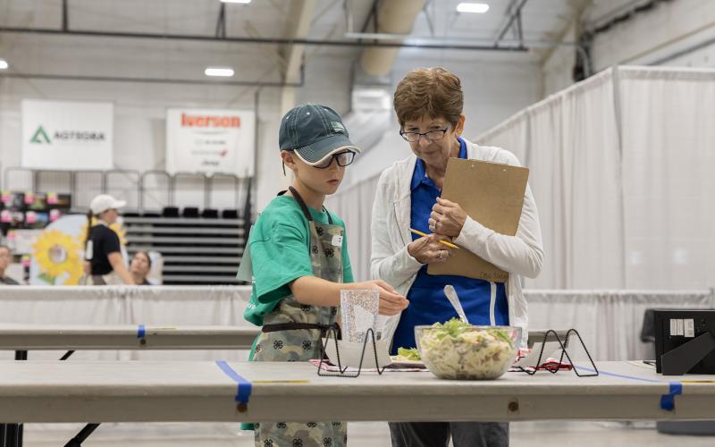 a boy wearing an apron talking with a judge infront of plated food