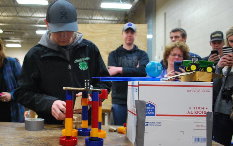 a boy working with blocks to build a machine to move a toy. He is standing infront of his classmates.