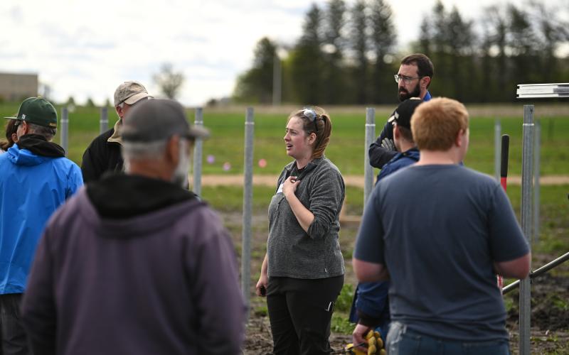 A woman with brown hair in a braid wearing a grey T-Shirt with an SDSU Extension logo stands in the middle of a group of people at a construction site