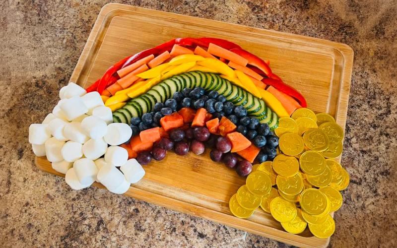 Variety of colorful fruits and vegetables arranged on a cutting board in the shape of a rainbow.