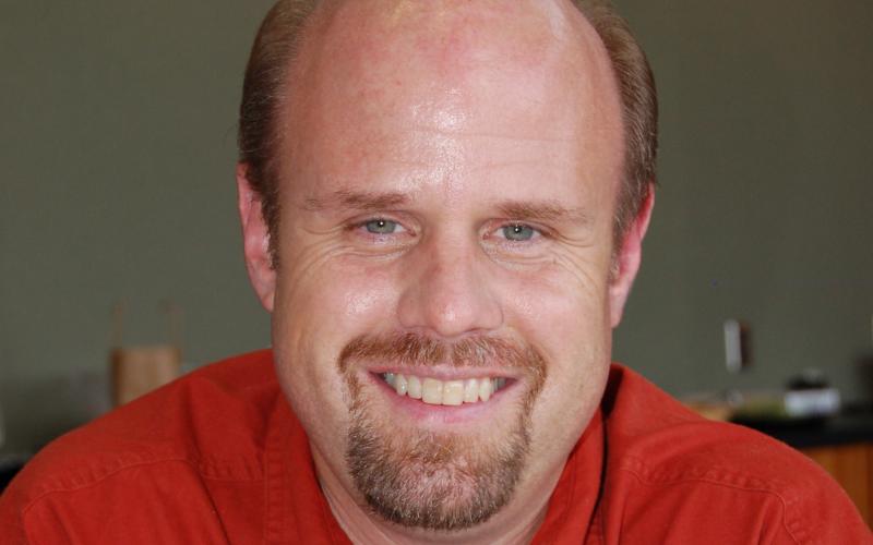 A mean in a red button-up shirt smiles for the camera