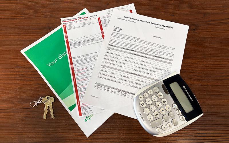 Insurance paperwork, calculator, and set of keys arranged on a desk.