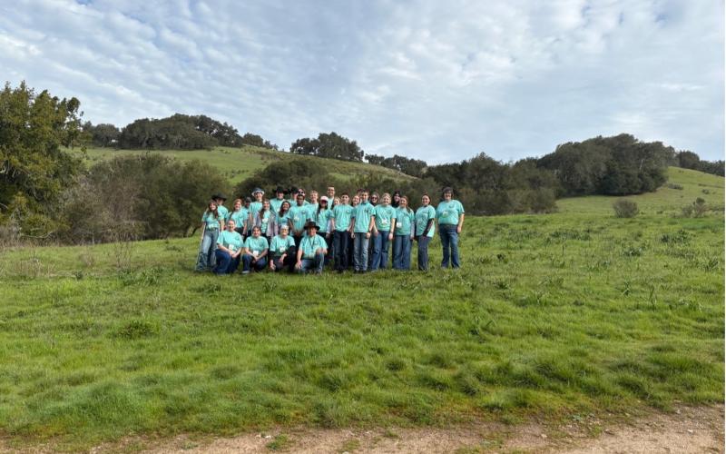 A group of people in an open pasture wearing light blue shirts smile for the camera