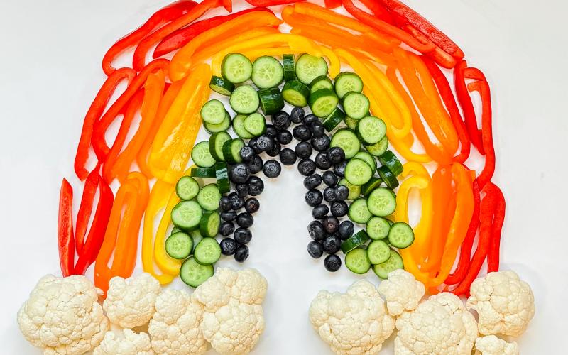 different colored fruits and vegetables arranged into a rainbow.