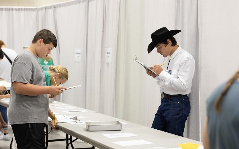two boys standing by a table with different objects on it with clip boards.