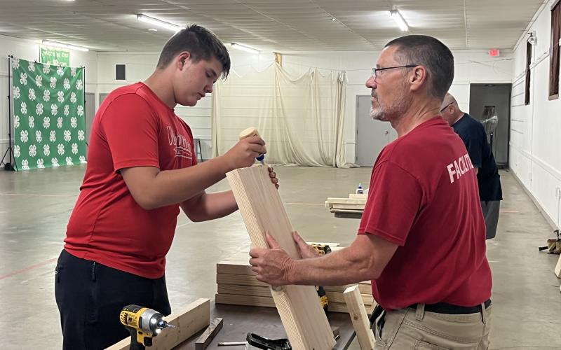 a man is holding a wood board as a youth boy adds wood glue to the end.