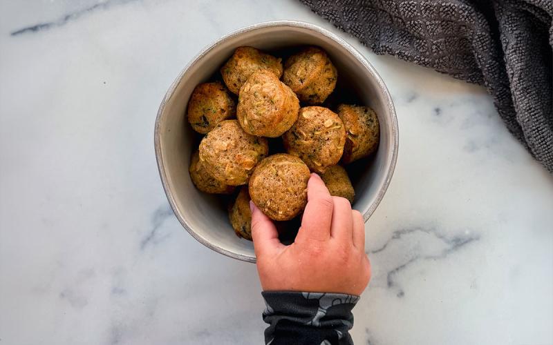 Hand grabbing a ready-made muffin from a bowl on a kitchen countertop.