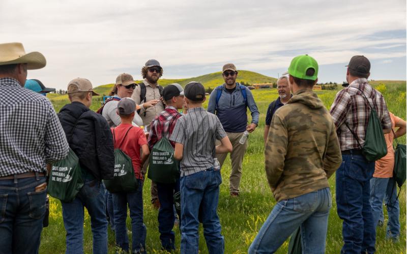 Youth stand outside in a pasture listening to an adult speak
