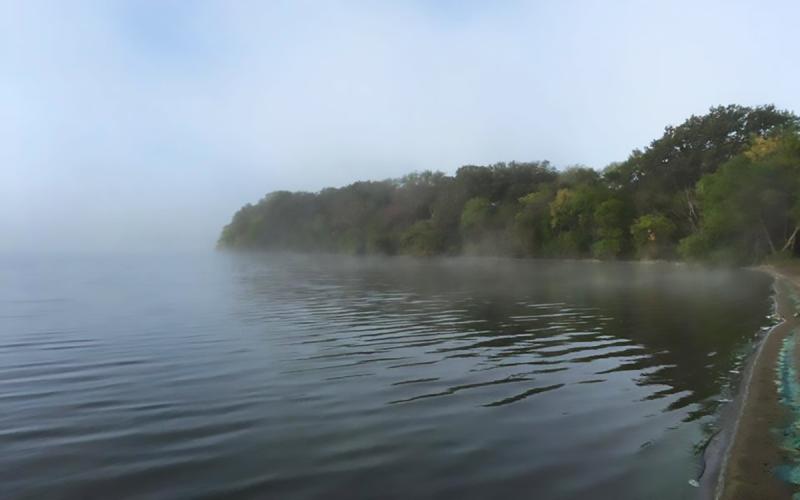 Fog rising over a wooded peninsula at Lake Herman.